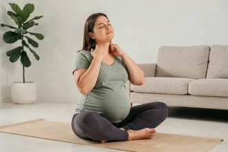 Femme enceinte au troisième trimestre massant les tensions de son cou en position assise sur un tapis de yoga dans un salon épuré