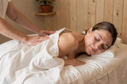 Femme adulte recevant un massage du dos dans un spa, allongée sur une table de massage en lin blanc, expression apaisée favorisant la détente et le sommeil